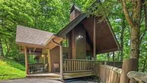 Un chalet rustique doté d’un porche couvert, d’un petit espace de détente extérieur et d’une clôture en bois.