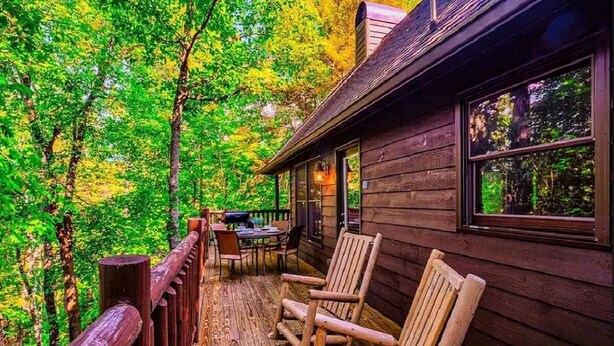 Une terrasse en bois avec une table et des chaises, entourée d’arbres.