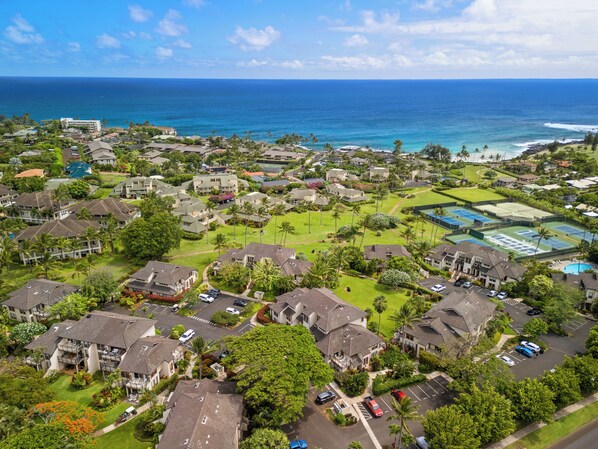 An aerial view of a coastal residential area with houses, a tennis court, and a view of the ocean.