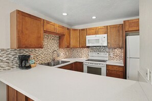 A kitchen with wooden cabinets, a microwave, stove, and a refrigerator. - Aston Poipu Kai Kauai 923 | Tropical Garden Views – Pool & Hot Tub (Koloa)