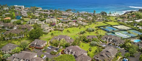 An aerial view of a coastal residential area with houses, a tennis court, and a view of the ocean.