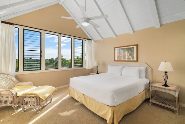 A bedroom with a large bed, a wicker chair, a nightstand, and a ceiling fan.