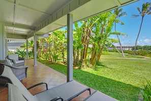 A covered outdoor seating area with wicker furniture and a view of a well-maintained lawn and palm trees.