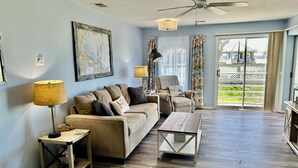 Un salon spacieux avec un canapé, une table basse et un fauteuil. Il y a une carte accrochée au mur et un ventilateur de plafond.