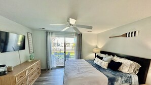 Une chambre à coucher comprenant un lit, une commode, un téléviseur, un ventilateur de plafond et une vue sur l’extérieur.