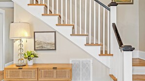 Una escalera con barandillas blancas y escalones de madera, una lámpara, un cuadro enmarcado y una pequeña mesa con una planta.