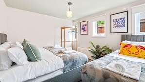 Ett hotellrum med två sängar, en garderob i trä, en klädstång och inramade konstverk på väggarna.