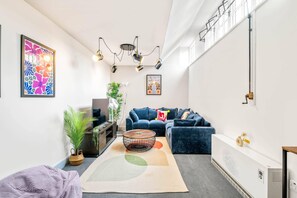 Un salon moderne avec un canapé bleu, une table basse ronde et un grand tableau abstrait accroché au mur.