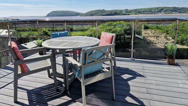 A deck with a round table and chairs, overlooking a beach and railway tracks. - 2br-sleeps4-balcony-petsok-parking-ferryside (Kidwelly)