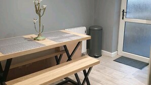 A dining table with a bench, a decorative vase, and a trash can in a room with a door and a radiator. - 2br-sleeps4-balcony-petsok-parking-ferryside (Kidwelly)