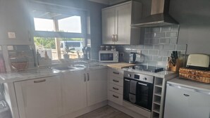 A modern kitchen with white cabinets, a microwave, an oven, and a sink. - 2br-sleeps4-balcony-petsok-parking-ferryside (Kidwelly)