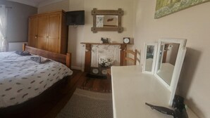 A bedroom with a bed, a wooden wardrobe, a television, a fireplace, and a mirror. - 3br-sleeps6-petsok-off Road Parking-garden (Kidwelly)