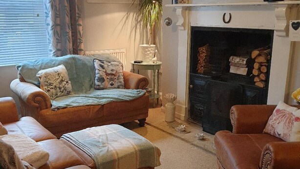 A cozy living room with leather sofas, a fireplace, a flat-screen TV, and a large window with curtains. - 3br-sleeps6-petsok-off Road Parking-garden (Kidwelly)