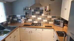 A compact kitchen with white cabinets, a gas stove, a microwave, and a sink. - 3br-sleeps6-petsok-off Road Parking-garden (Kidwelly)