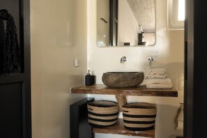 A bathroom with a wooden vanity, a large mirror, a round sink, and two striped baskets. - PanDa Art Houses (Mykonos)