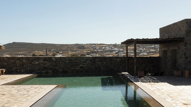 Piscina com borda de pedra e muro de pedra ao fundo.