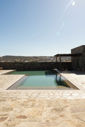 A pool with a stone border and a stone wall in the background. - PanDa Art Houses (Mykonos)