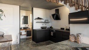 Uma cozinha moderna com armários pretos, bancada de pedra e uma ilha grande. Há um exaustor preto sobre o fogão e uma TV de tela plana na parede.