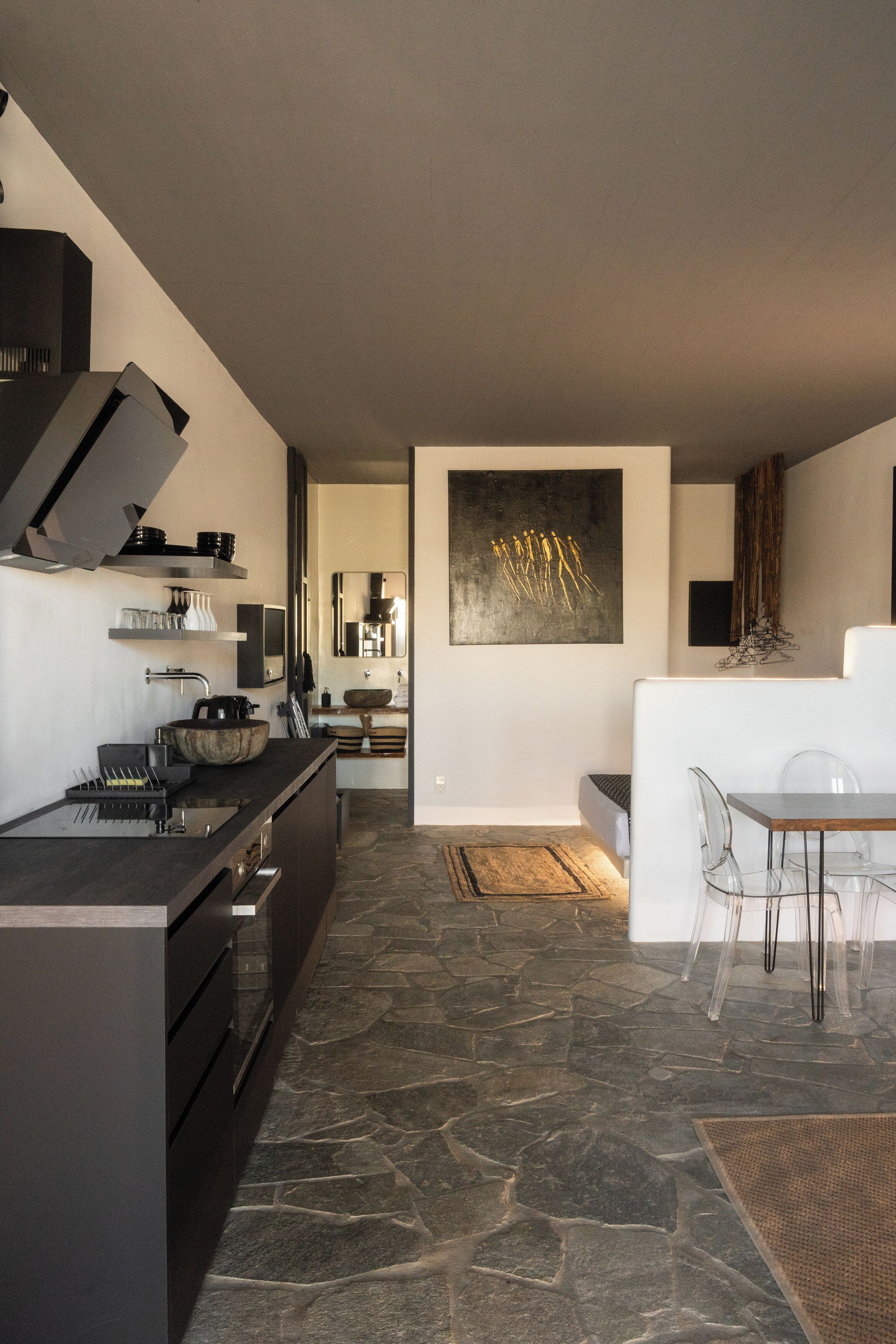 Une cuisine moderne avec un sol en pierre, un coin repas doté de chaises transparentes et un grand tableau abstrait accroché au mur.