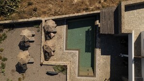 Vista aérea de uma área de piscina com paredes de pedra, cercada por guarda-sóis e assentos.