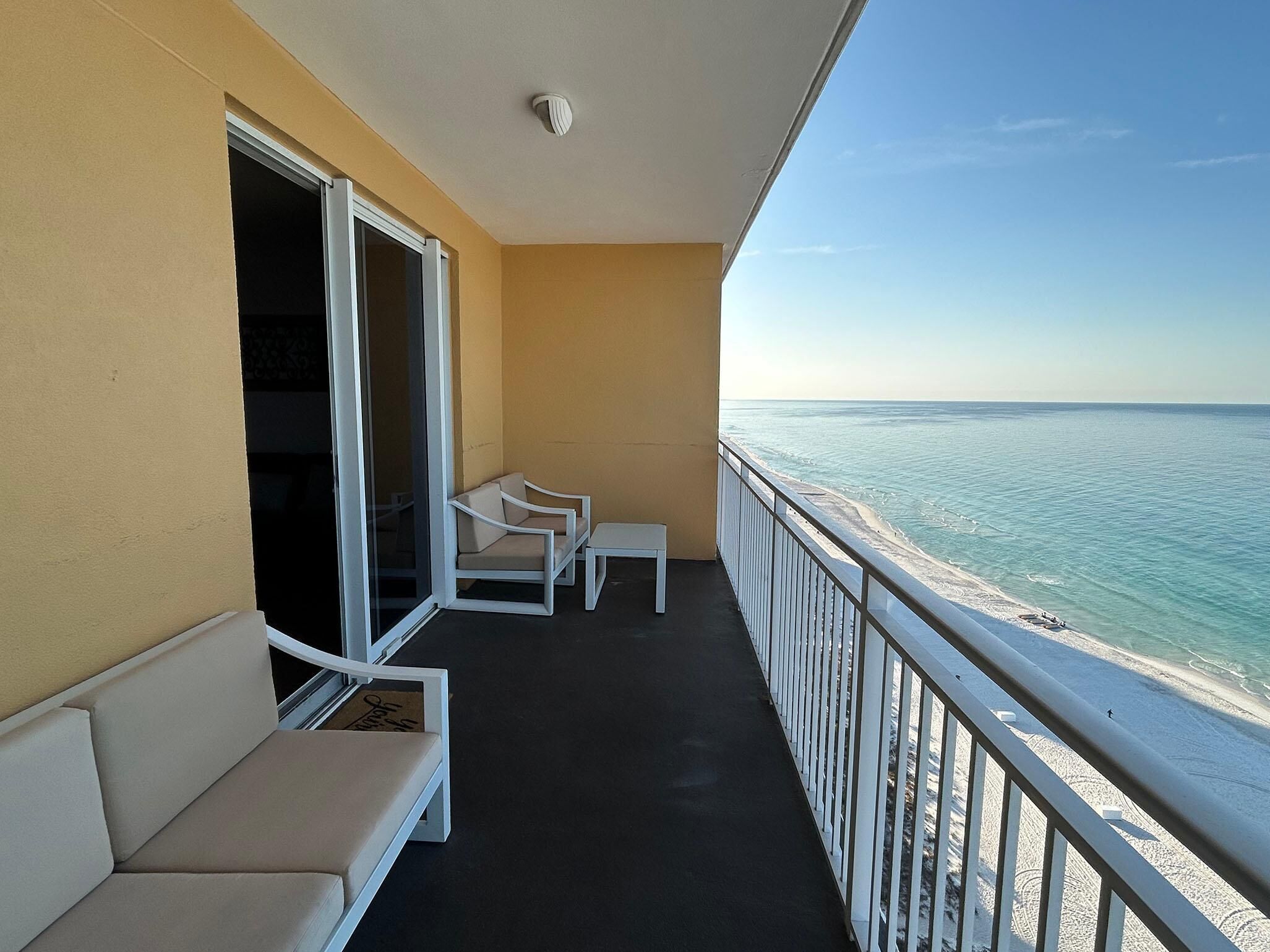 A balcony with a view of the beach, a sofa, and a small table.