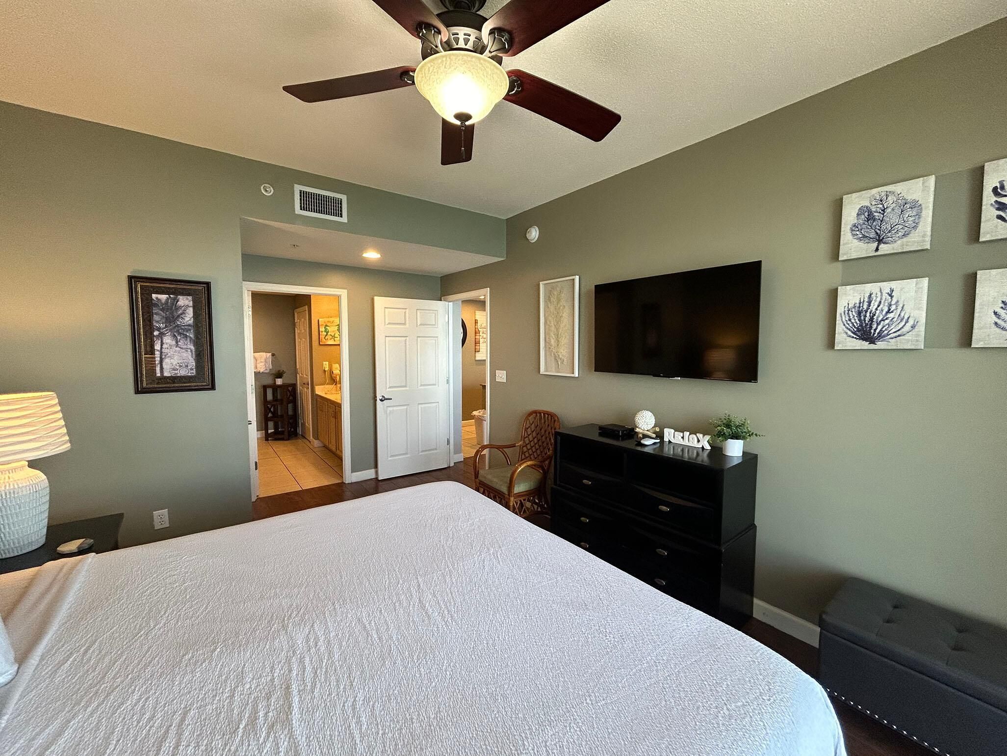 A bedroom with a bed, a ceiling fan, a TV, and artwork on the wall.