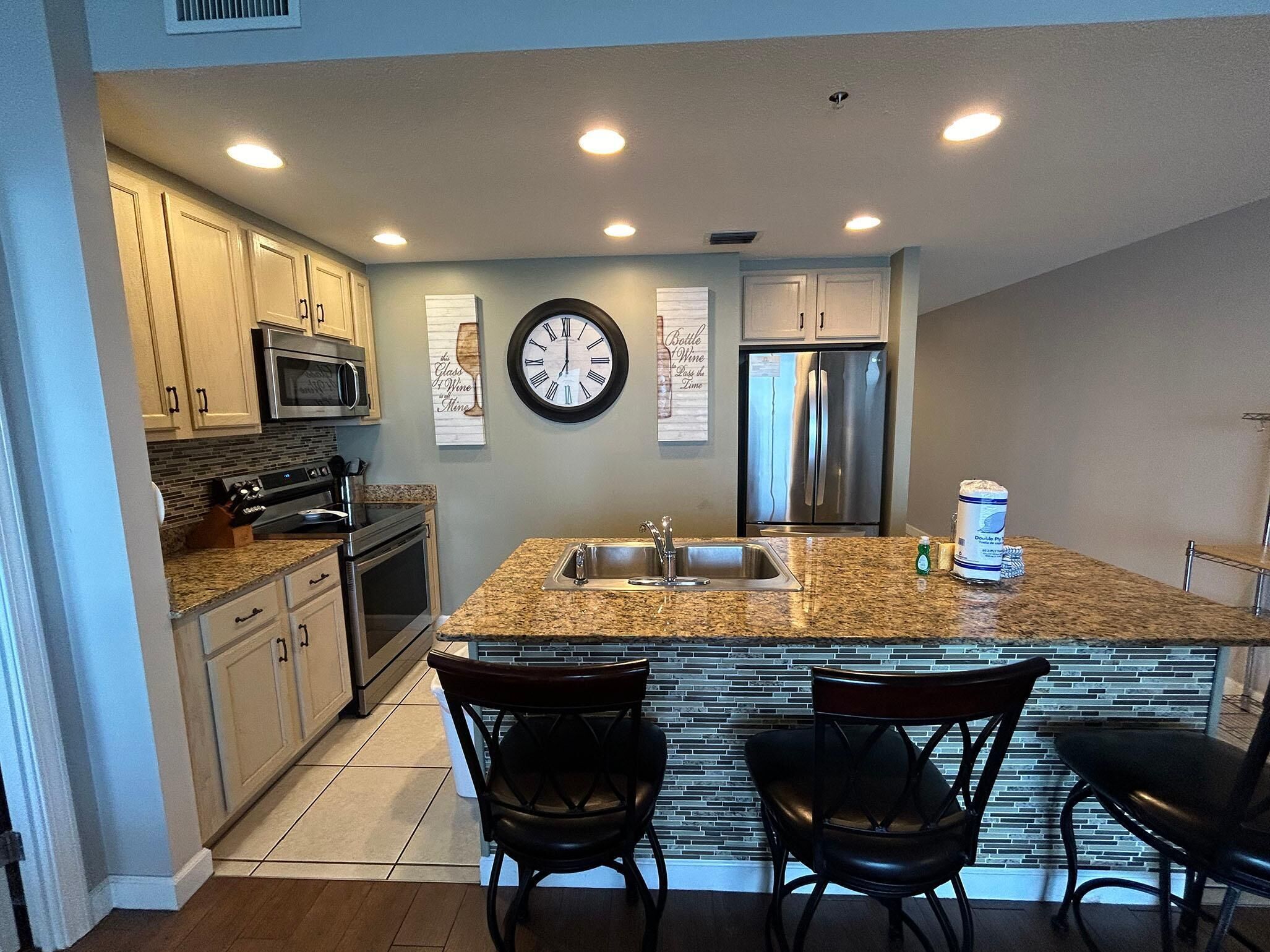 A modern kitchen with granite countertops, stainless steel appliances, and a central island with bar stools.