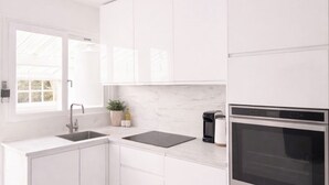 A modern kitchen with white cabinetry, a built-in oven, and a window providing natural light. - Maison Calme en Bordure de Forêt (Le Perray-en-Yvelines)