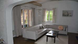 A modern living room with a white sectional sofa, a dark coffee table, and a large window with curtains. - Faïza  - Four Bedroom Villa, Sleeps 8 (Roquebrune-sur-Argens)