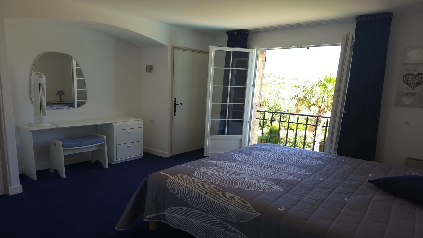 Een slaapkamer met een bed, bureau, stoel, kledingkast en een balkon met uitzicht op groen.