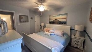 A bedroom with a bed, nightstands, a ceiling fan, a painting, and a mirror.