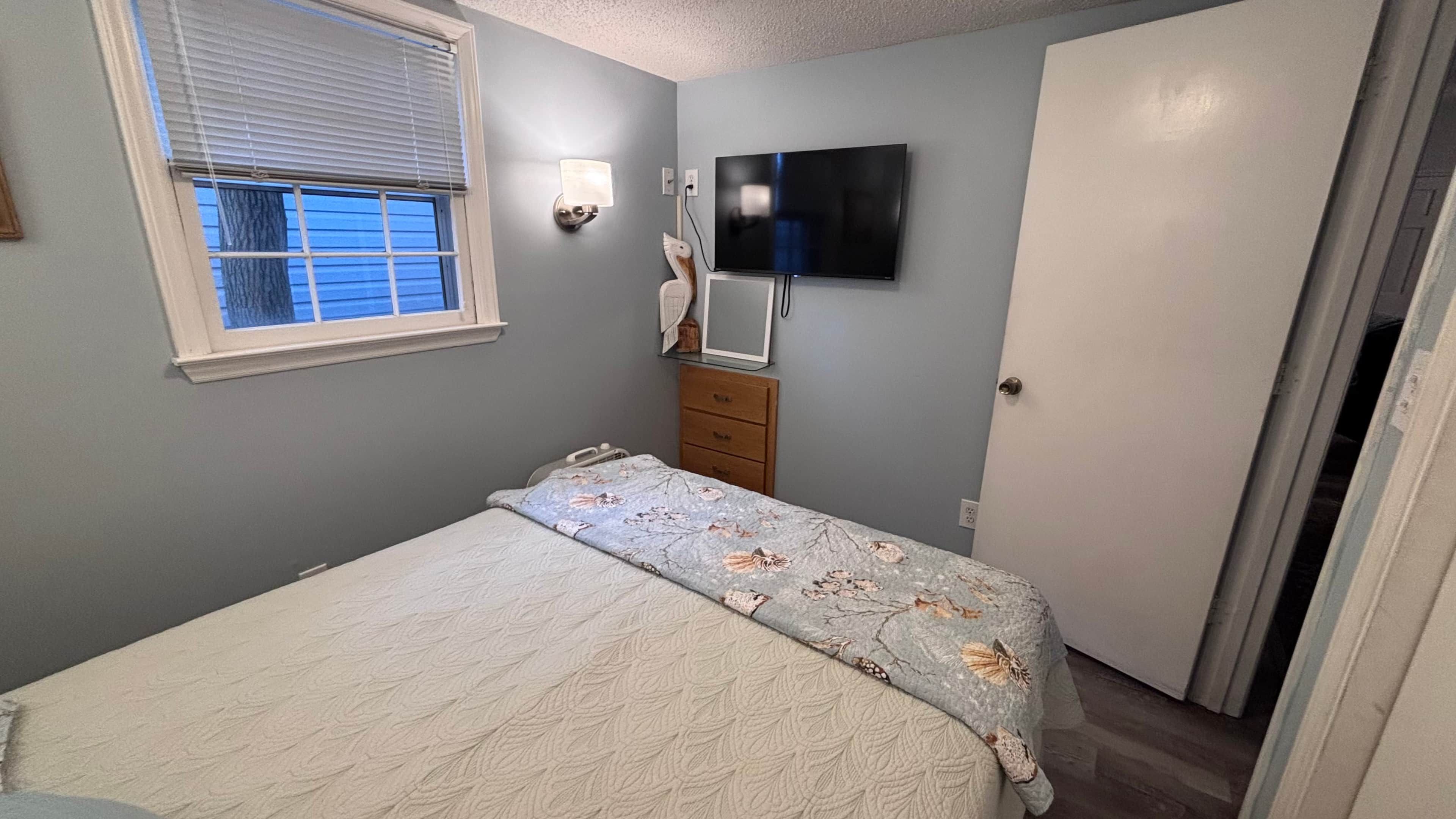 Quarto com cama, penteadeira, televisão e janela.