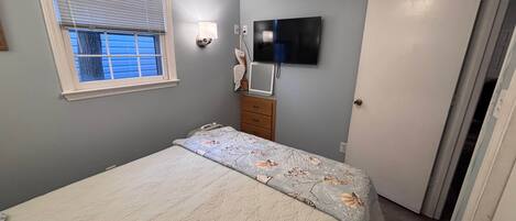 Quarto com cama, penteadeira, televisão e janela.