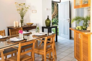 A dining area with a glass table, wooden chairs, and a wooden cabinet with a plant.
