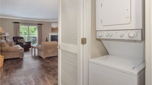 A laundry room with a front-loading washer and dryer, a wooden floor, and a seating area with two sofas and a chair. - Walk-in Level | 2 BR | Balcony | Sleeps 6 | Free Tickets (Pigeon Forge)