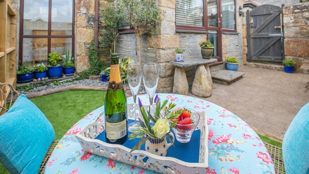 A table set outdoors with a bottle of champagne, glasses, and a tray with strawberries and a vase of flowers. - 1 bedroom accommodation in Newquay (Newquay)