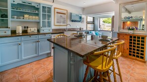 A kitchen with light blue cabinets, a central island with bar stools, a window with a view, and a tiled floor. - 1 bedroom accommodation in Newquay (Newquay)
