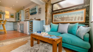 A cozy living room with a teal sofa, wooden coffee table, and a stone wall. - 1 bedroom accommodation in Newquay (Newquay)