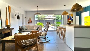 A modern kitchen with a dining area, a rocking chair, and a large window overlooking a garden. - Casa Marcel, 4 Chambres, 4 Sdb, Décoration Bohème, au Calme Dans la Pinède (La Tremblade)
