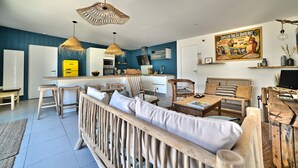 A modern living room with a sofa, chairs, a coffee table, and a kitchen area in the background. - Casa Marcel, 4 Chambres, 4 Sdb, Décoration Bohème, au Calme Dans la Pinède (La Tremblade)