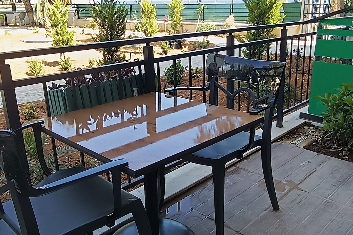 A balcony with a table and chairs, a green fence, and some plants.