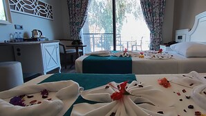 A hotel room with two beds, a desk with a kettle, and a view of the outdoors.