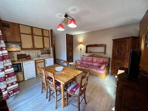 A compact kitchen with wooden cabinets, a dining table with chairs, and a red patterned sofa.