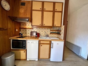 A compact kitchen with wooden cabinets, a built-in oven, a dishwasher, and a refrigerator.