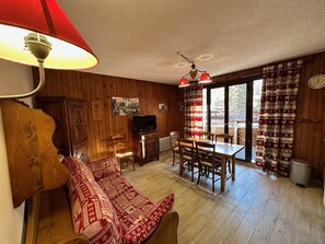 Un salon confortable avec un canapé, un téléviseur, une table à manger avec des chaises et une fenêtre avec des rideaux.
