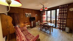Tunnelmallinen olohuone, jossa on sohva, televisio, puuseinät sekä ruokailutila tuoleineen ja pöytineen.