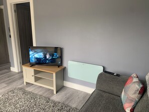 Ein Wohnzimmer mit Fernseher auf einem Holzständer, einer Couch und einem gemusterten Kissen.