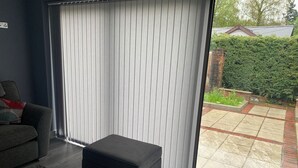 A modern living room with a grey sofa, a black ottoman, and a large sliding glass door leading to a patio with a brick floor and greenery. - Impeccable 1-bed House in Aberdare (Aberdare)