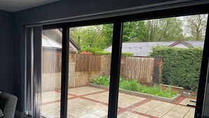 A modern room with a large sliding glass door leading to a patio with a tiled floor, a wooden fence, and a hedge. - Impeccable 1-bed House in Aberdare (Aberdare)