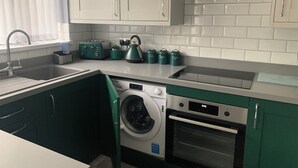 A compact kitchen with a washing machine, an oven, a toaster, and a kettle. - Impeccable 1-bed House in Aberdare (Aberdare)